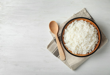 Bowl of boiled rice and spoon on wooden background, top view with space for text