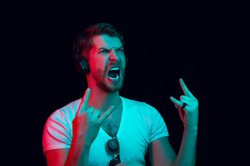 Enjoying his favorite music. Happy young stylish man with headphones listening sound and smiling while standing against blue neon background