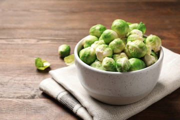 Bowl of fresh Brussels sprouts and napkin on wooden table. Space for text