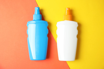 Bottles with sun protection body cream on color background, top view