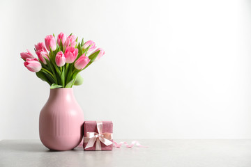 Bouquet of beautiful spring tulips in vase and gift box on table against white background. International Women's Day