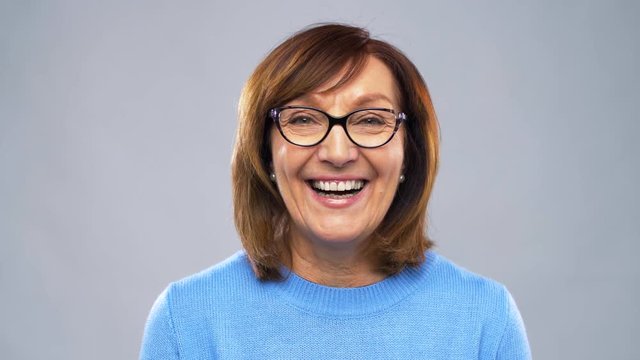 emotion, age and people concept - portrait of happy senior woman in glasses over grey background