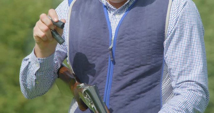 A clay Pigeon shooter breaks the barrels of his double barrelled shotgun and the cartridges fly out in slow motion.
