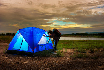 Young women survey around at evening lit tent in camping by nature with mountain and lake background, Open lamp in the tent at night on campground in forest.
