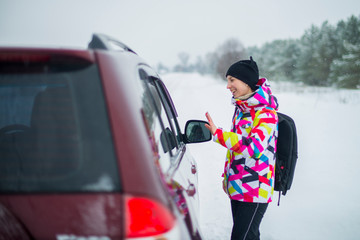 Beautiful girl in a bright ski jacket catches the car on the winter road