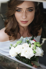 attractive caucasian bride with a bouquet sitting in a wedding car and smile to the camera