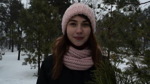 Portrait of a girl in a hat on the background of dark pine branches in winter.