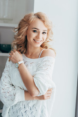 Smiling curly woman in white knitted sweater looking at camera