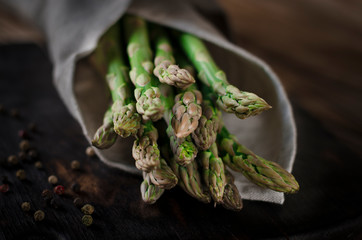 Green juicy asparagus is lying on a wooden board on a brown wooden table.