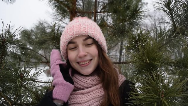 Portrait of a young girl in a hat on the background of Christmas tree branches in winter.
