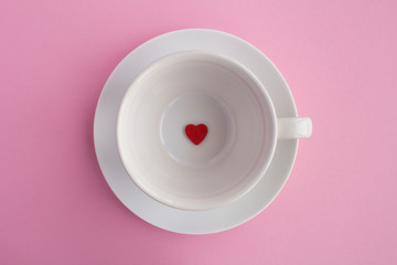 Small red heart on the empty white cup on the pink background .Top view.Copy space.Diet minimal concept.