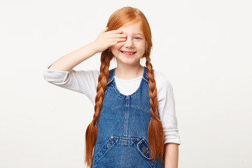 Smiling glad red-haired girl at the reception at the oculist, covered left eye with a palm, the second looks at the camera, names the written letters, has good eyesight, isolated on white