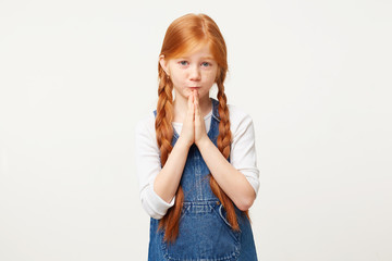 Hoping wishing something, red-haired kid folded arms in a prayer gesture. Girl with braids want...