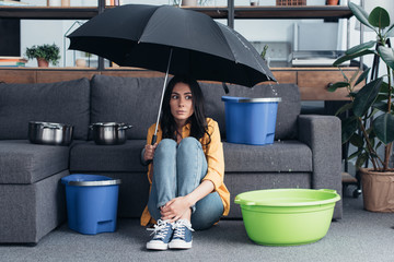 Confused girl sitting under umbrella in living room