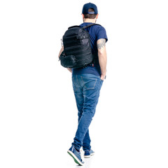 Fototapeta premium A man photographer in jeans and cap, black backpack goes walking on white background isolation, back view