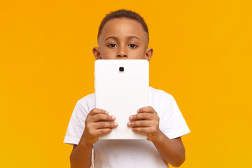 Picture of smart dark skinned schoolboy holding generic white digital tablet, doing homework,...