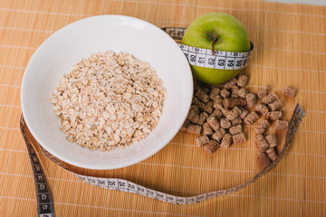 Green apple wrapped by a centimeter. Bran and oatmeal in a plate. Healthy food. Diet for weight loss. Dietary bread