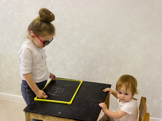 Older sister plays with junior to school. The teacher tells about the skills of reading and...