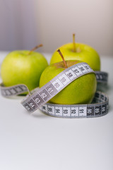 A green apple wrapped with a centimeter lies on a white table. Apple diet