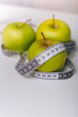 A green apple wrapped with a centimeter lies on a white table. Apple diet