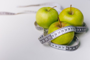 A green apple wrapped with a centimeter lies on a white table. Apple diet