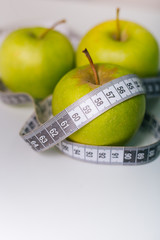 A green apple wrapped with a centimeter lies on a white table. Apple diet