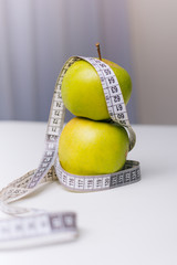 A green apple wrapped with a centimeter lies on a white table. Apple diet