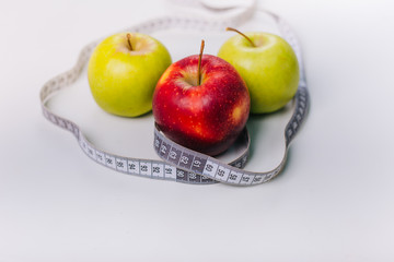 Three red and green apples wrapped with a centimeter lie on a white table. Apple diet.