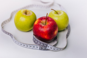 Three red and green apples wrapped with a centimeter lie on a white table. Apple diet.