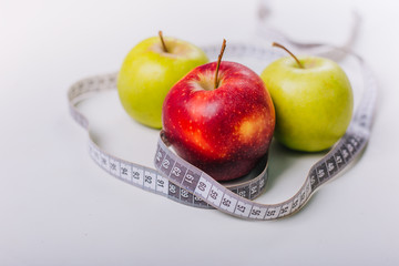 Three red and green apples wrapped with a centimeter lie on a white table. Apple diet.