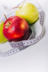 Three red and green apples wrapped with a centimeter lie on a white table. Apple diet.