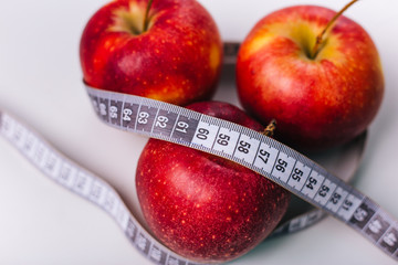 Red apple wrapped centimeter lies on a white table. Apple diet