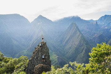 Three adventurous hikers climbing a rocky pinnacle in the junle of Reunion Island - 249382997