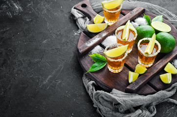 Gold tequila with lime and salt on black stone background. Top view. Free space for your text.