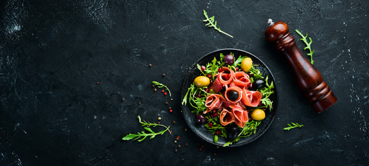 Salad with Prosciutto, olives and arugula. Cold snacks. Top view. Free space for your text.