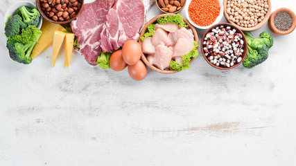 Food high in protein on table. Meat, chicken fillet, broccoli, beans, cheese, eggs, wheat. On a white wooden background.