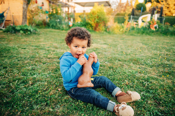 Adorable two year old african toddler boy eating chocolate bunny on backyard