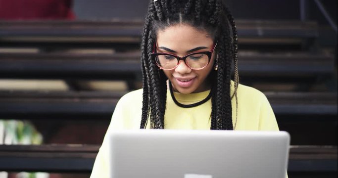 Good looking african lady using her bank card using her laptop to check or to buy something online , she wearing a eyeglasses , in the middle of office hall she sitting down on the stairs