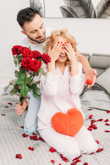 Man making proposal and presenting flowers to girlfriend in bedroom