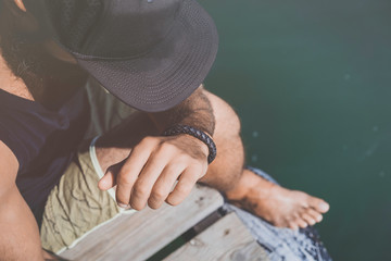 Bearded man model wearing black cap and tshirt looks away, sunset in the sea scenery. Close up portrait. Sunlight effect