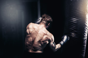 Fototapeta na wymiar Strong and muscular guy practicing punching the boxing bag. Moody environment. Edgy edit style.