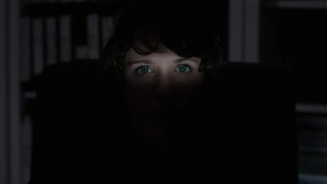 A Young woman's eyes are spotlighted in light in a dark shadowy environment