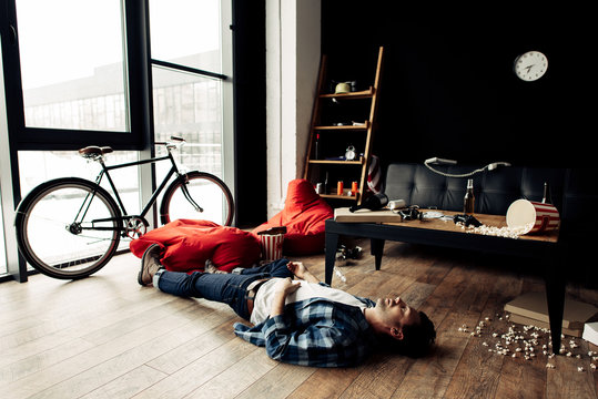 drunk man lying on floor in messy living room after party