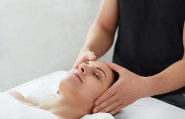 Fototapeta na wymiar Young beautiful woman enjoying anti-aging facial massage.Male therapist making head massage to female client.Professional masseur.Relaxation,beauty,spa,body and face treatment concept.