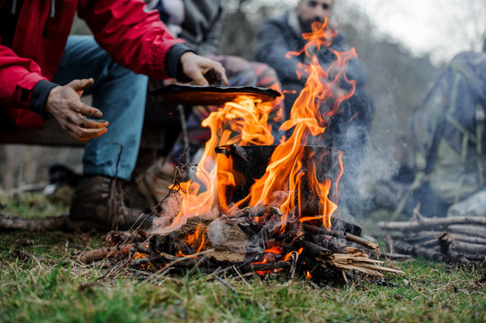 Boy In A Red Jacket Placing A Cover On The Black Pan Standing On The Bonfire