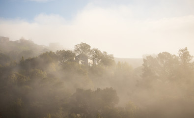 Large house on hilltop surrounded by mist and trees at sunrise