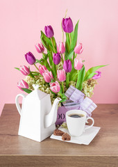 Bouquet of fresh tulips and porcelain coffee set on a wooden table.