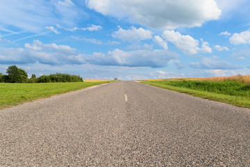 Straight road extending beyond the horizon to a beautiful blue sky with ornate clouds.