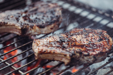 selective focus of juicy spicy steaks grilling on barbecue grid with smoke
