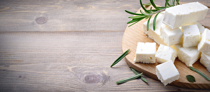 Feta cheese with rosemary on wood background. Top view with space for text
